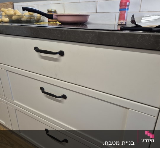 מגירות מטבח עם ידיות שחורות וסיר על השיש